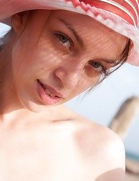 Arina wears a wide-brimmed hat while out nude sunbathing